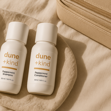 Two bottles of dune + kind shampoo and conditioner on a beige fabric background