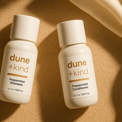 Two bottles of dune + kind Peppermint Shampoo and Conditioner on a beige background