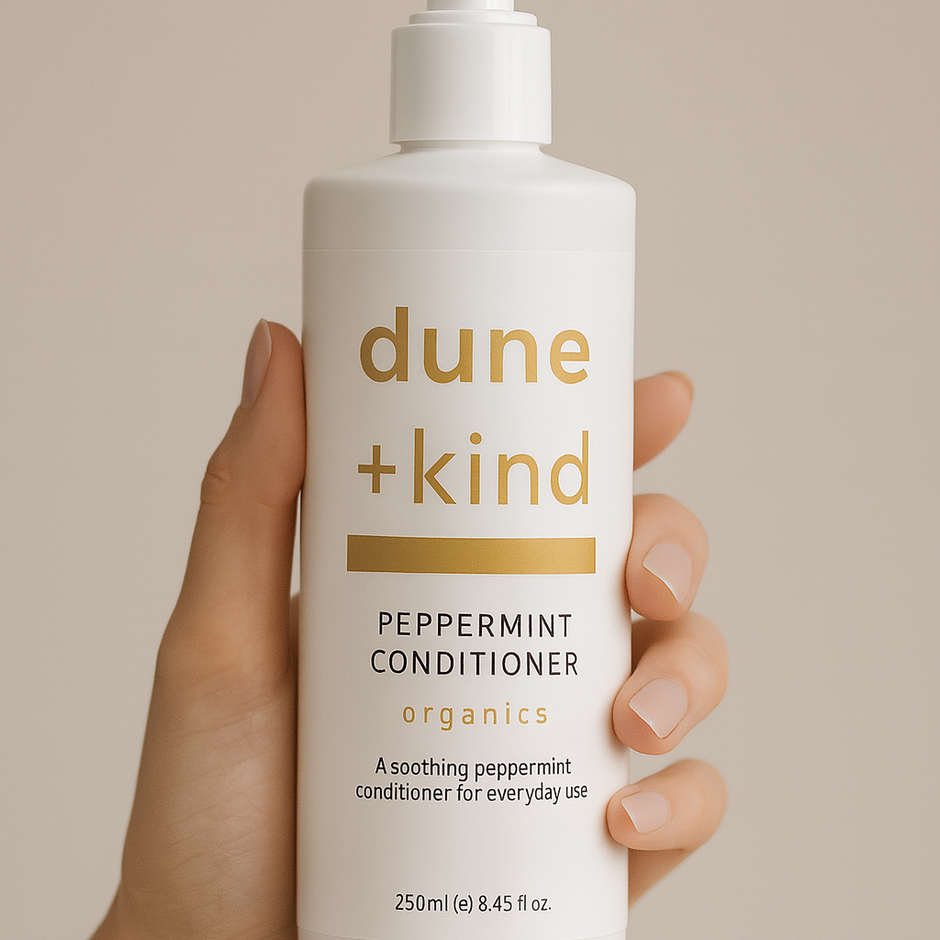 Hand holding a bottle of dune + kind peppermint conditioner against a beige background