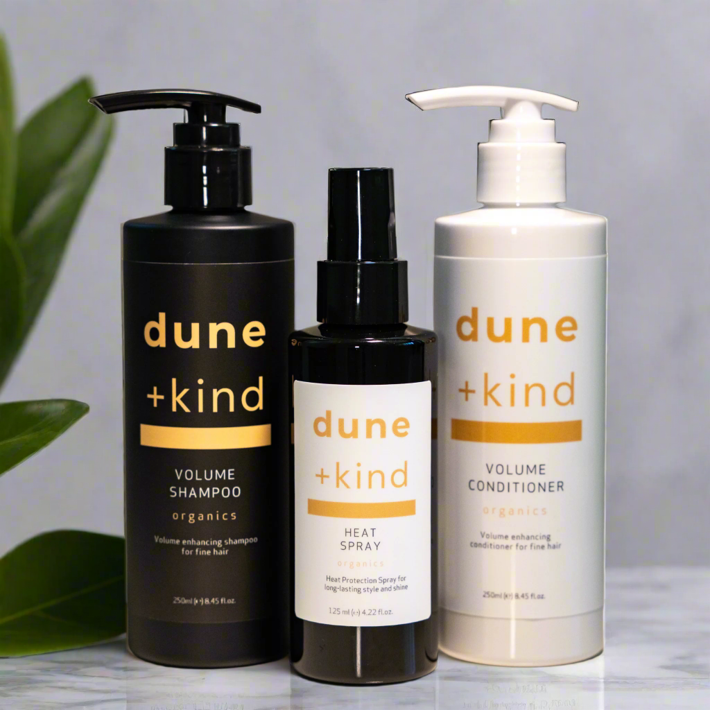 Three bottles of dune + kind hair care products on a neutral background