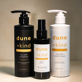 Three bottles of dune + kind hair care products on a neutral background