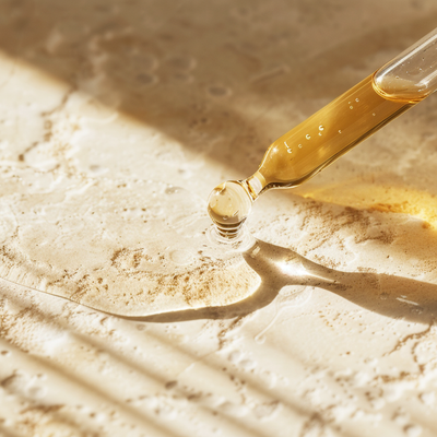 Gold dropper with liquid on a textured beige surface