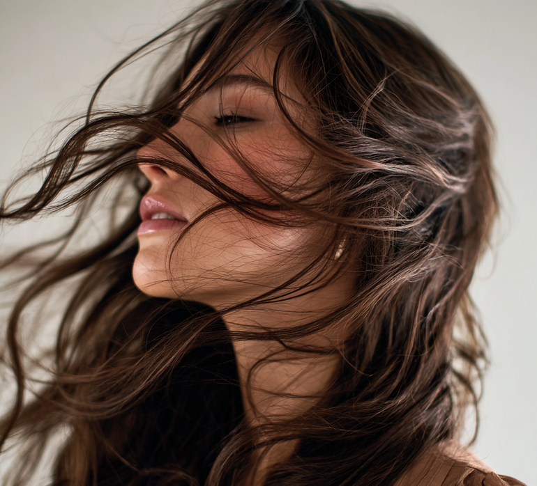 Woman with long brown hair blowing in the wind against a neutral background